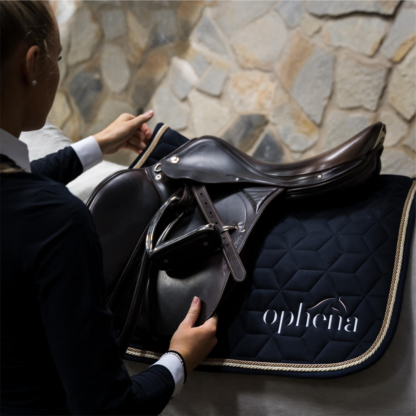 Rider fixing her saddle, fitted with an Ophena Saddle Pad and Ophena S stirrups